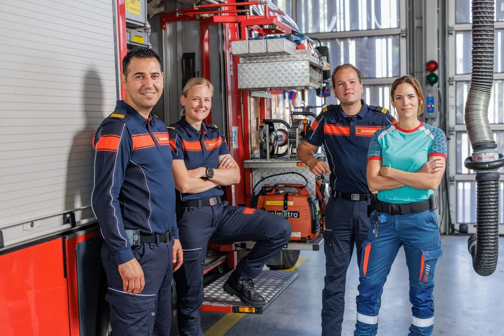 Vier collega’s van de brandweer en de ambulancezorg staan samen in de kazerne bij de tankautospuit.